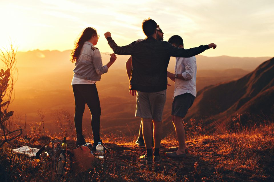 Vier Freunde stehen im Sonnenuntergang am Berg.