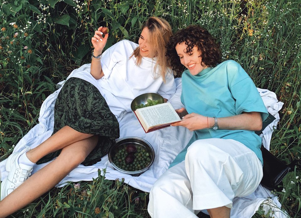 Zwei Frauen liegen zum Picknick auf einer Decke im Gras.