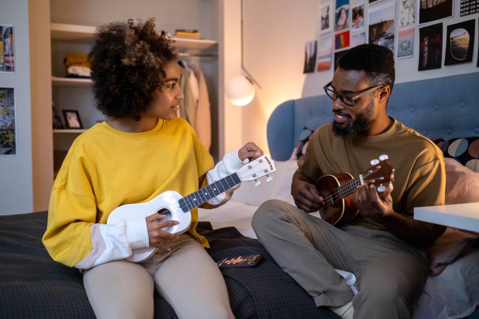 Mann und Mädchen sitzen am Bett und spielen mit ihren Gitarren.