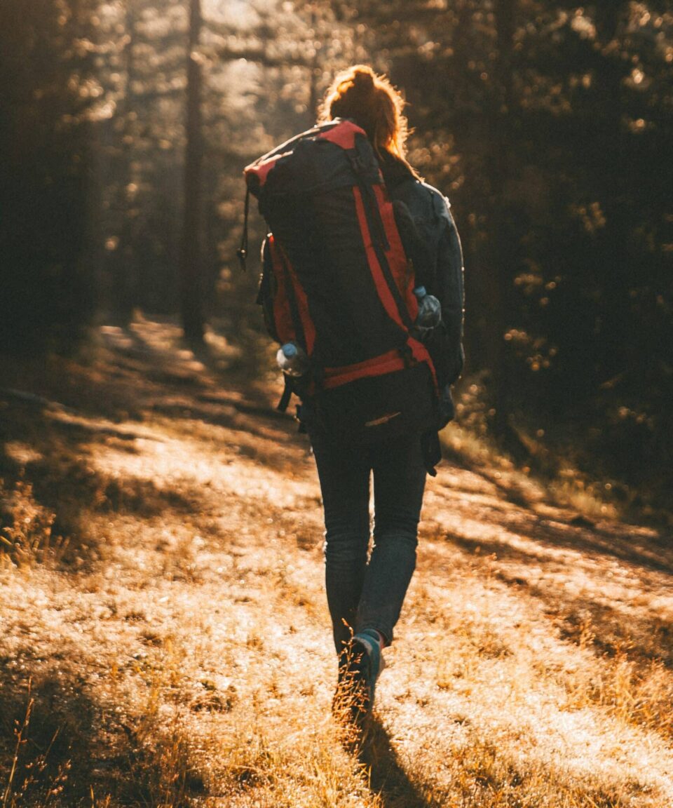 Frau geht mit großem Rucksack durch den Wald