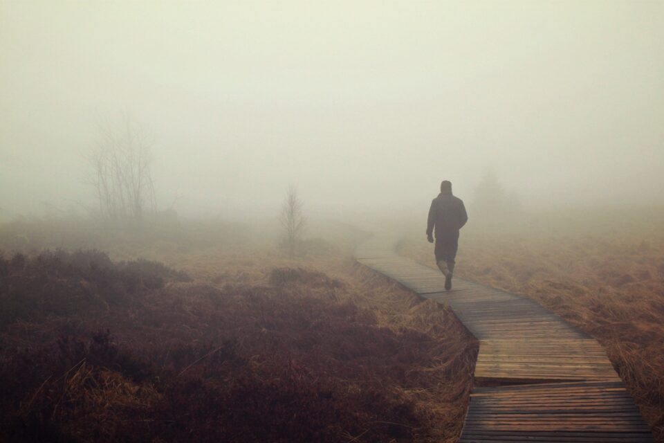 Mann geht auf Holzweg durch einen nebligen Sumpf