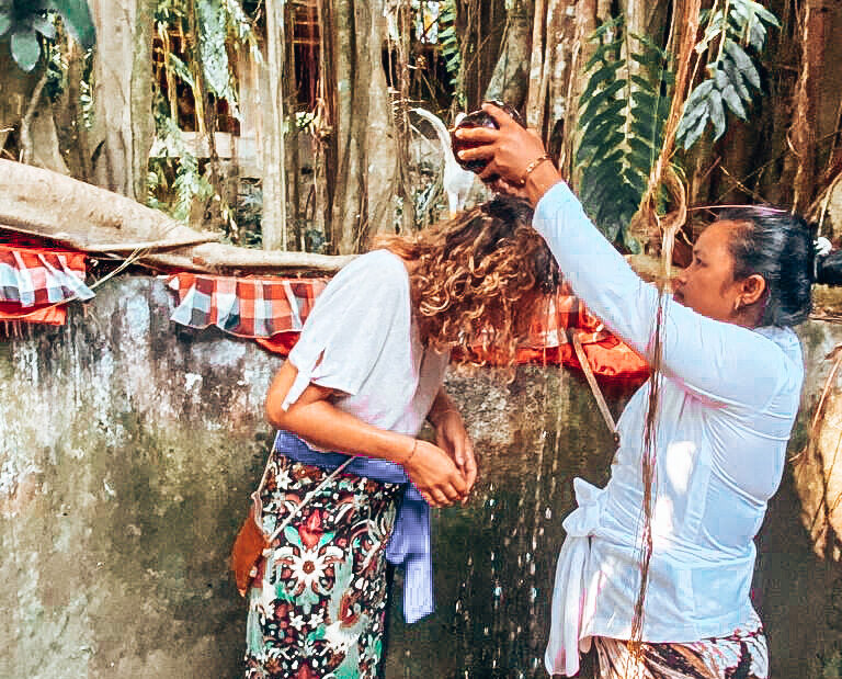 Birgit wird auf Bali von einer Frau mit Wasser überschüttet