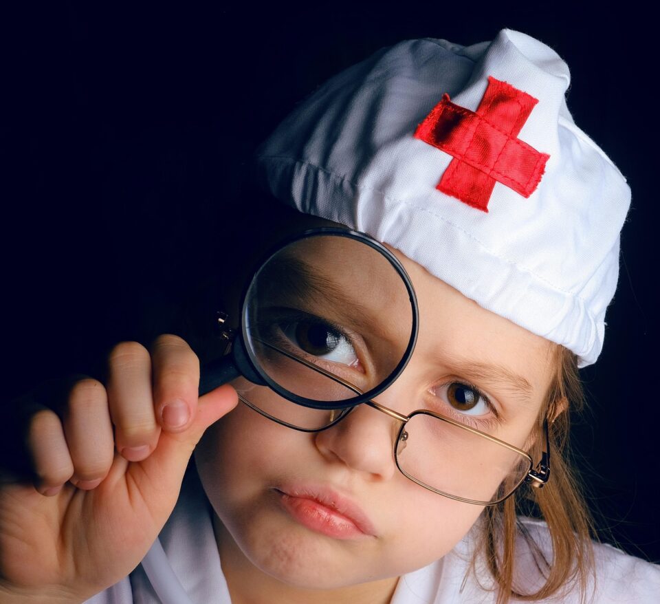 Kind, als Krankenschwester verkleidet, mit Lupe.