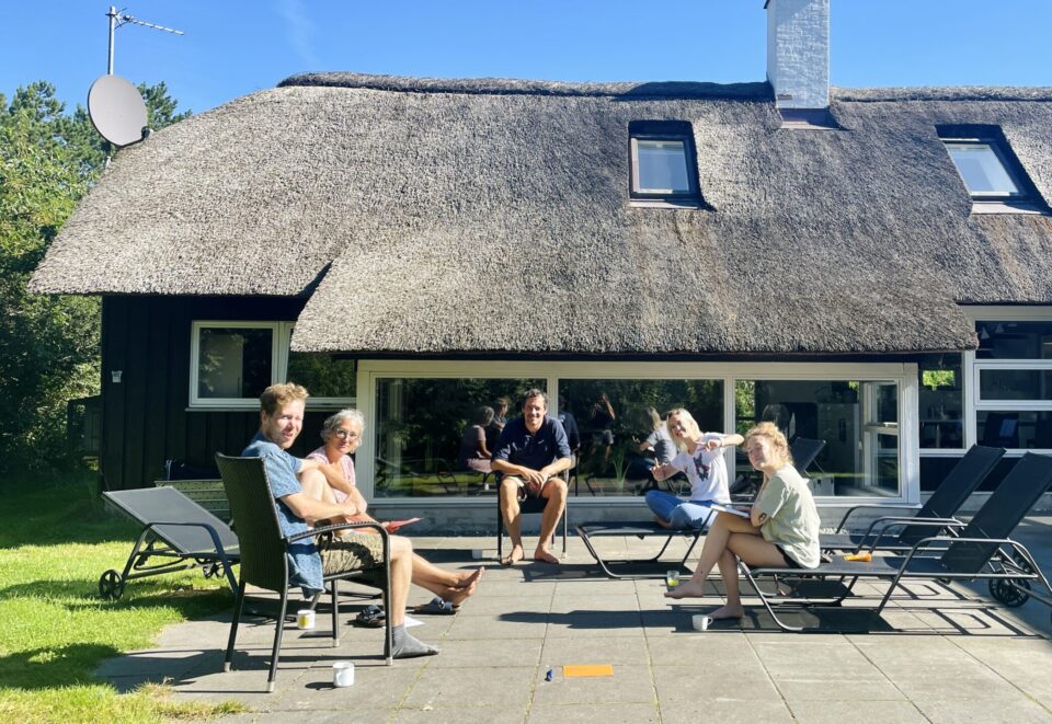 Das Kurvenkratzer-Team auf Strandliegen vor einem Haus mit Reetdach.