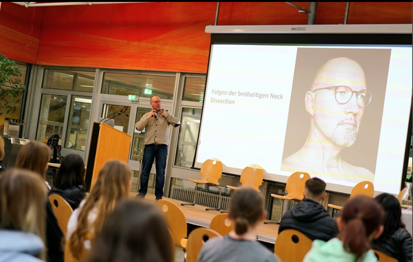 Don als Vortragender auf der Bühne vor einem Publikum.